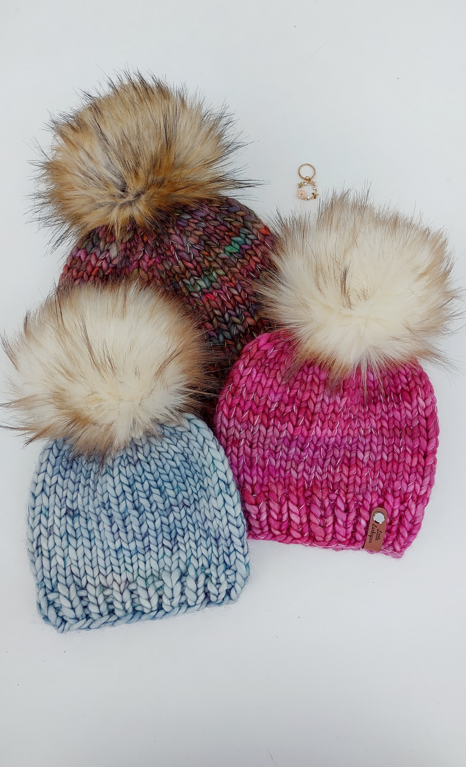 Three colorful hats with big faux fur pom poms