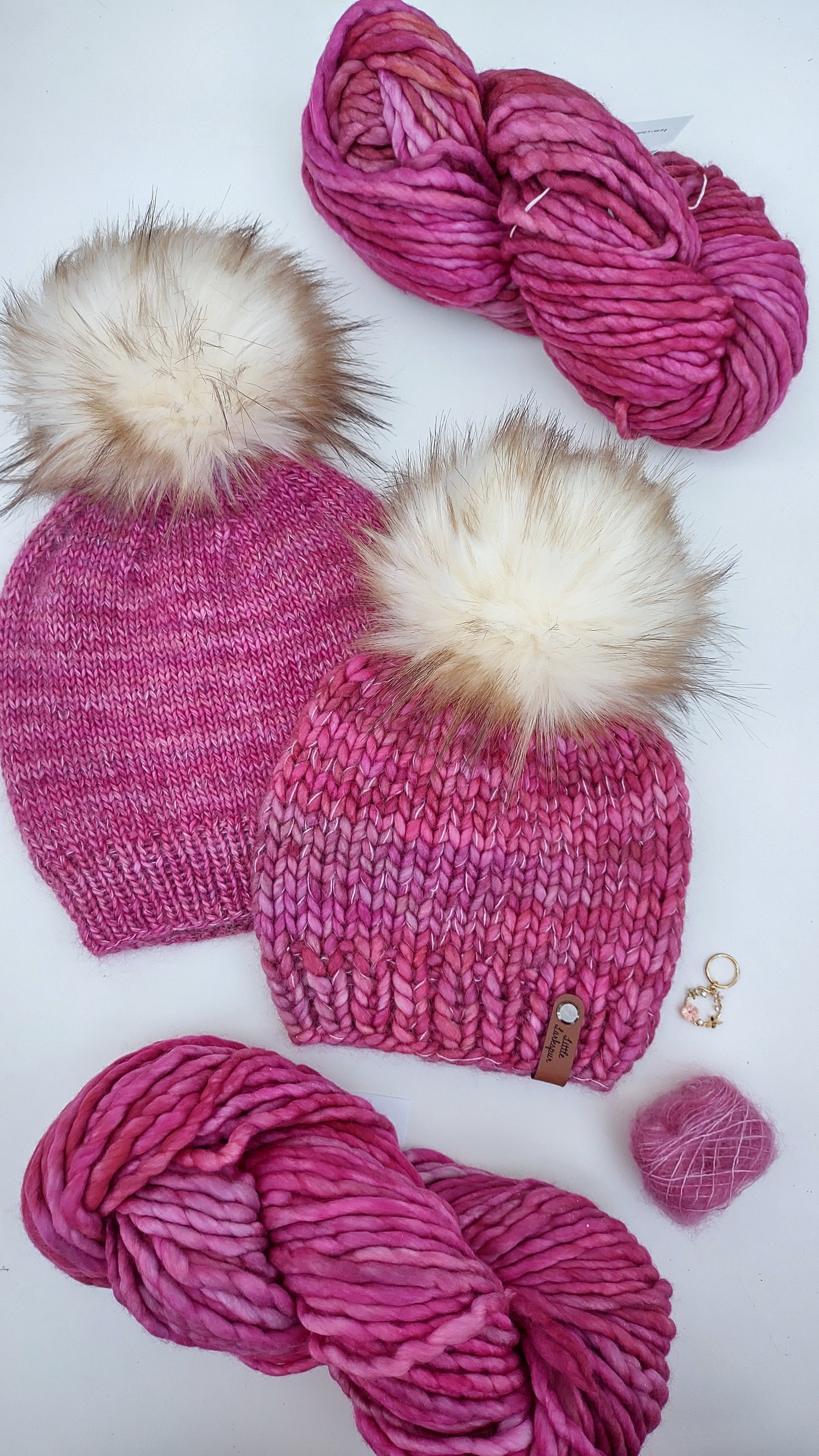 Two bright pink hats with big faux fur pom poms
